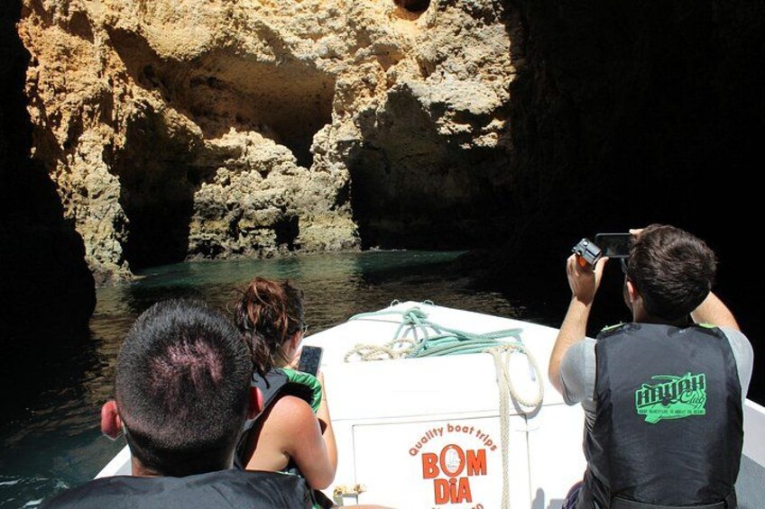 A boat with people taking photos, surrounded by rocky cliffs and water. 5