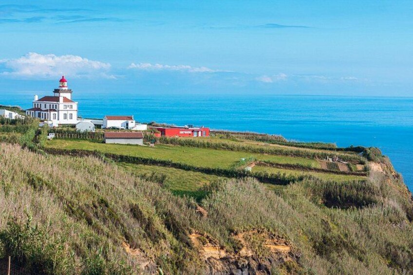 A coastal landscape with a lighthouse, grassy fields, and a clear blue sky. 3