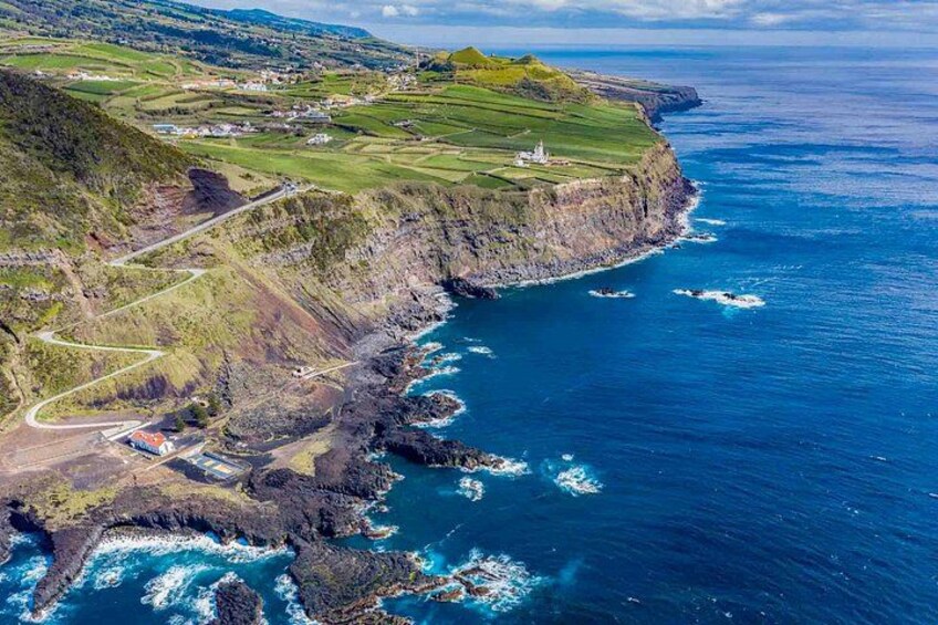 A coastal landscape with cliffs, a winding road, and a lighthouse. 5