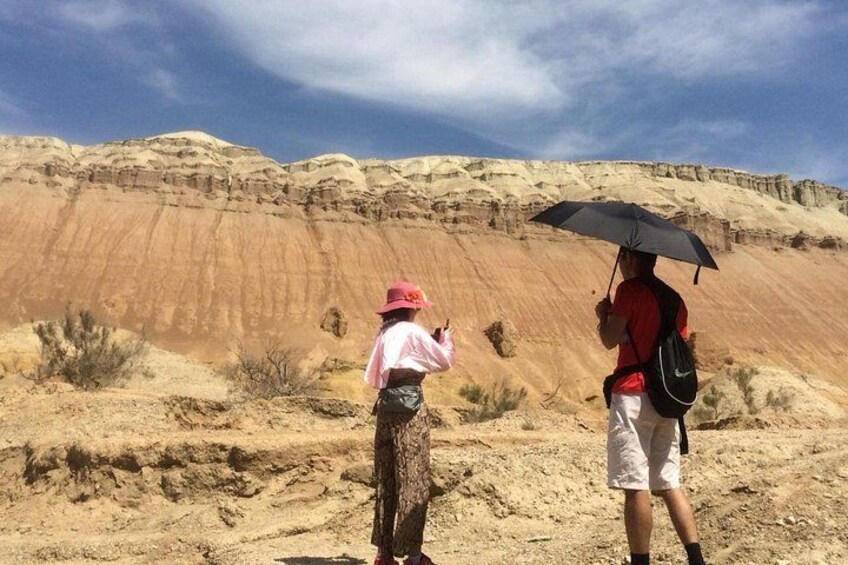 Two people standing in a desert with a rocky cliff in the background. 1