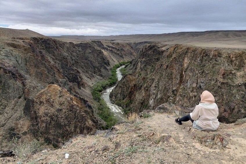 A canyon with a river, rocky terrain, and a person sitting on the edge. 5