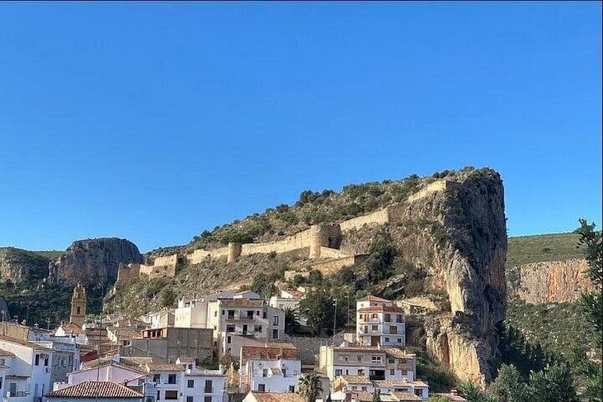 Un pueblo con edificios en una colina, un acantilado destacado y un cielo azul despejado. 3