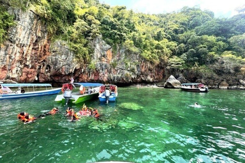 A group of people swimming in a clear river surrounded by cliffs. 1