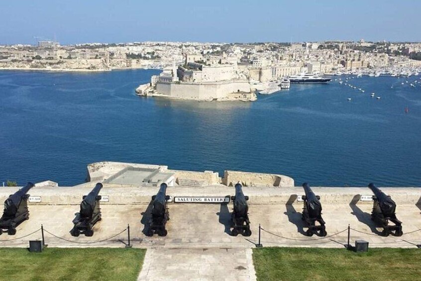 A coastal cityscape with a fortified harbor, cannons on display, and a clear sky. 3