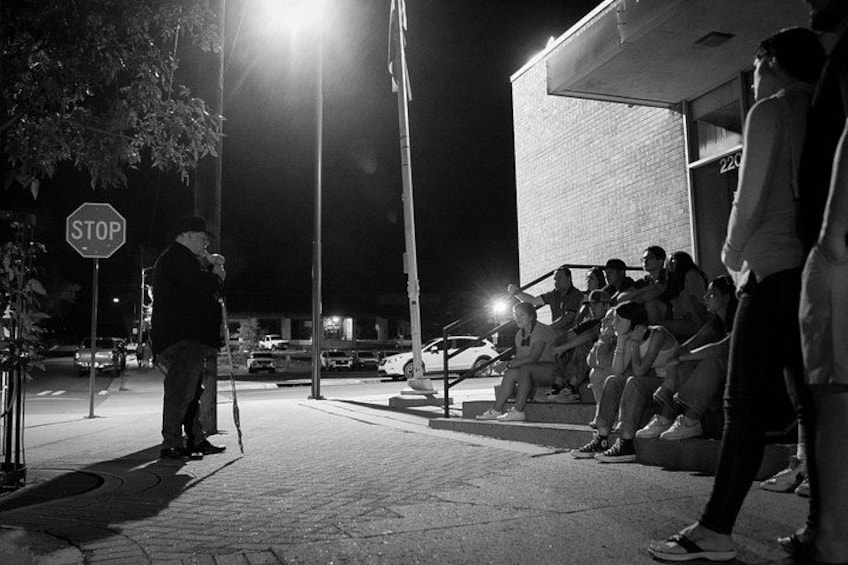 A nighttime street scene with a stop sign, a group of people sitting on a bench, and a building in the background. 2