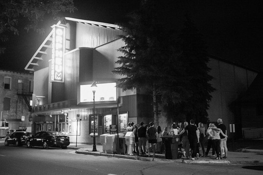 A building with a marquee sign, a group of people standing outside, and a street lamp. 3