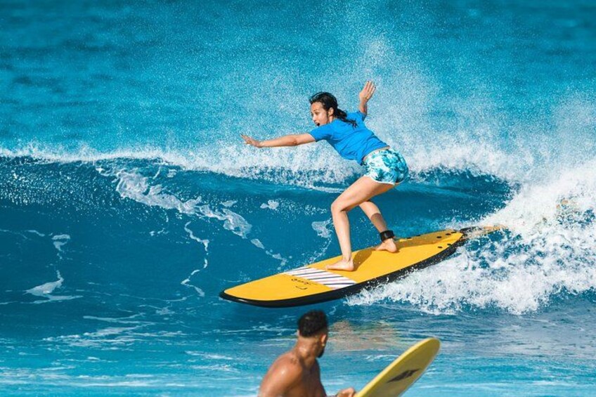 Une personne fait de la planche à vague sur une planche jaune dans une piscine, une autre personne se trouvant à l'arrière-plan. 1