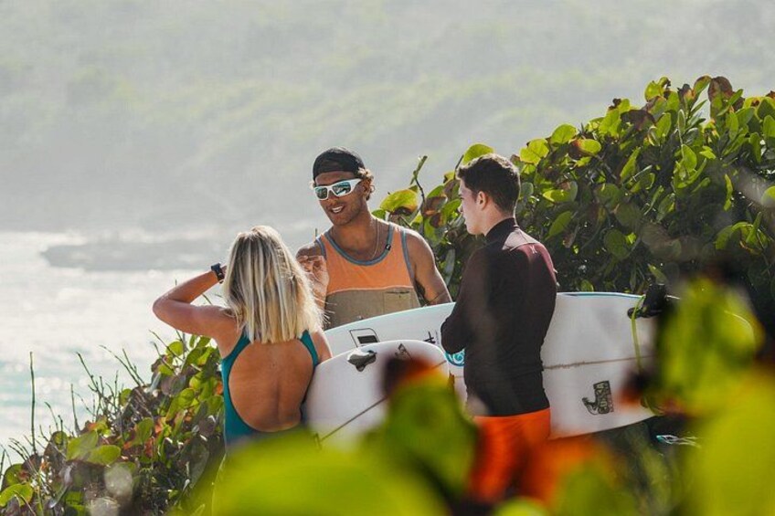 Trois personnes, équipées de planches de surf, se trouvent près d’une zone côtière, avec une végétation luxuriante et l’océan en arrière-plan. 4