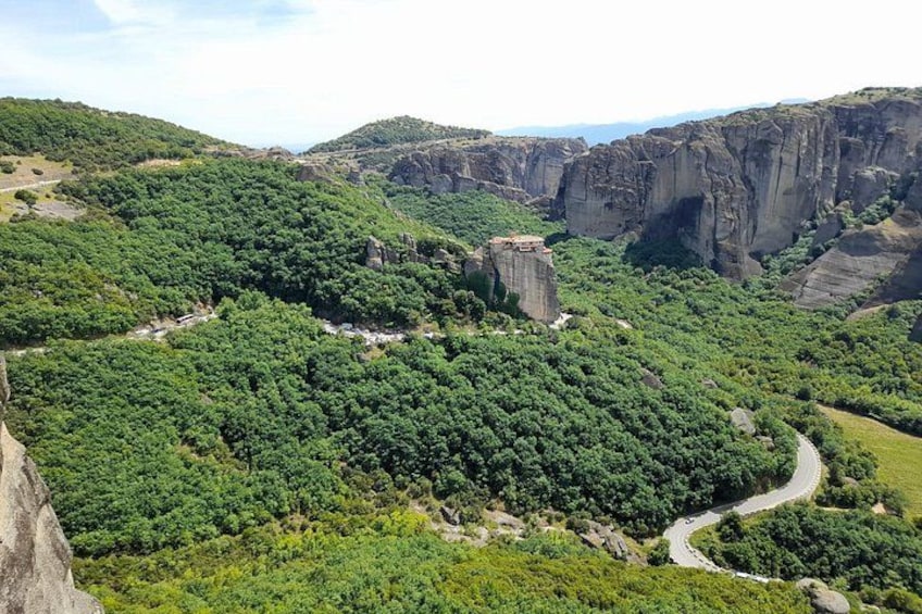 Un paisaje montañoso con densos bosques verdes, un camino serpenteante y una formación rocosa destacada. 4