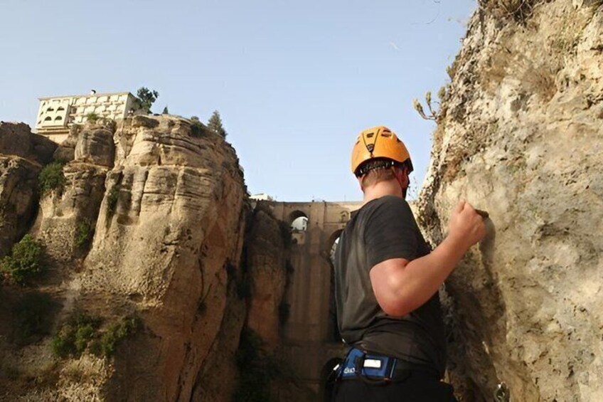 A person rappelling down a rocky cliff with a building in the background. 5