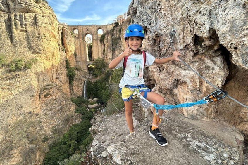 A person rock climbing on a rocky cliff with a bridge in the background. 1