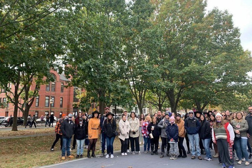A group of people standing in a park with trees and a building in the background. 3