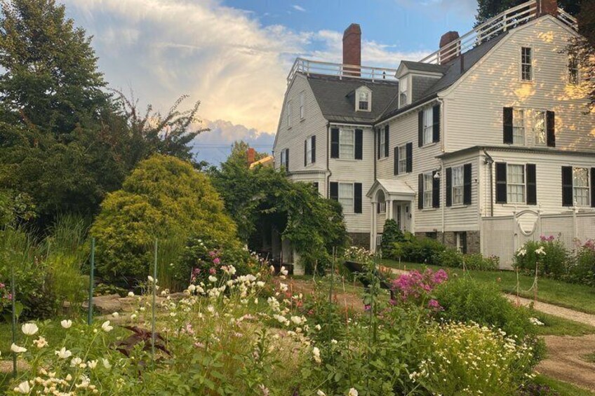 A row of white houses with black shutters, surrounded by a garden with various flowers and greenery. 5