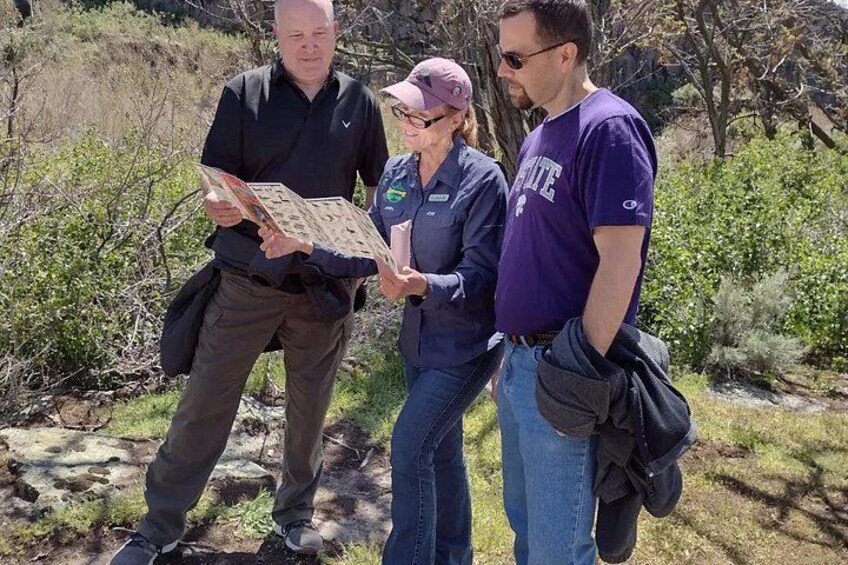 Three people outdoors, one holding a map, standing on a rocky path with vegetation around. 4