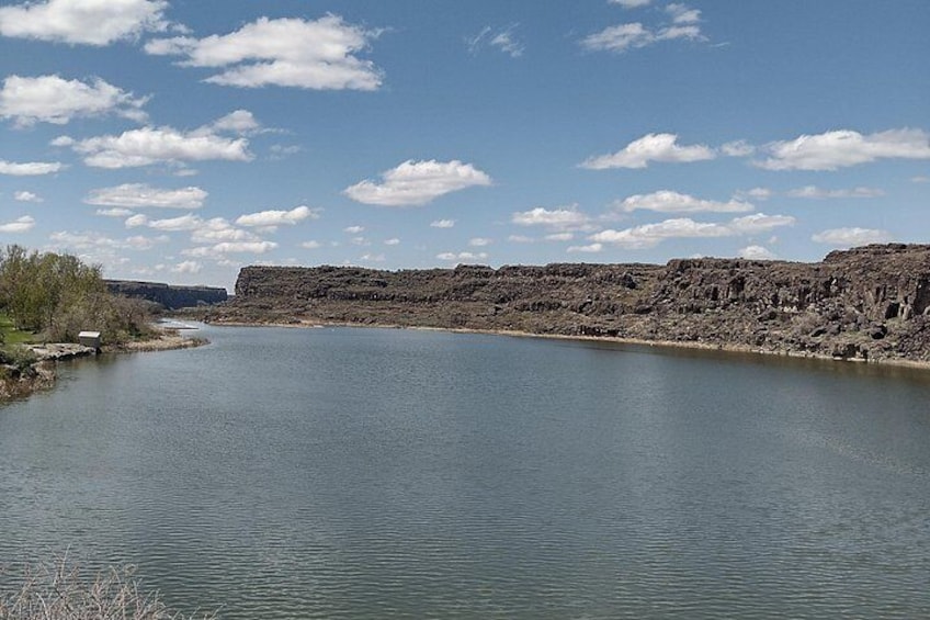 A river with a rocky cliff on the right and a small boat on the left. 2