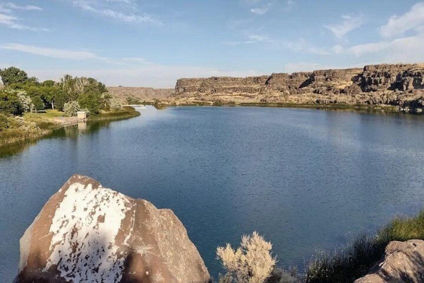 A calm river with rocky banks, a large boulder in the foreground, and a clear sky. 4
