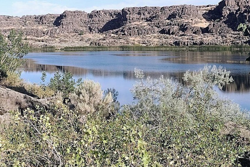 A calm lake surrounded by rocky terrain and sparse vegetation. 3