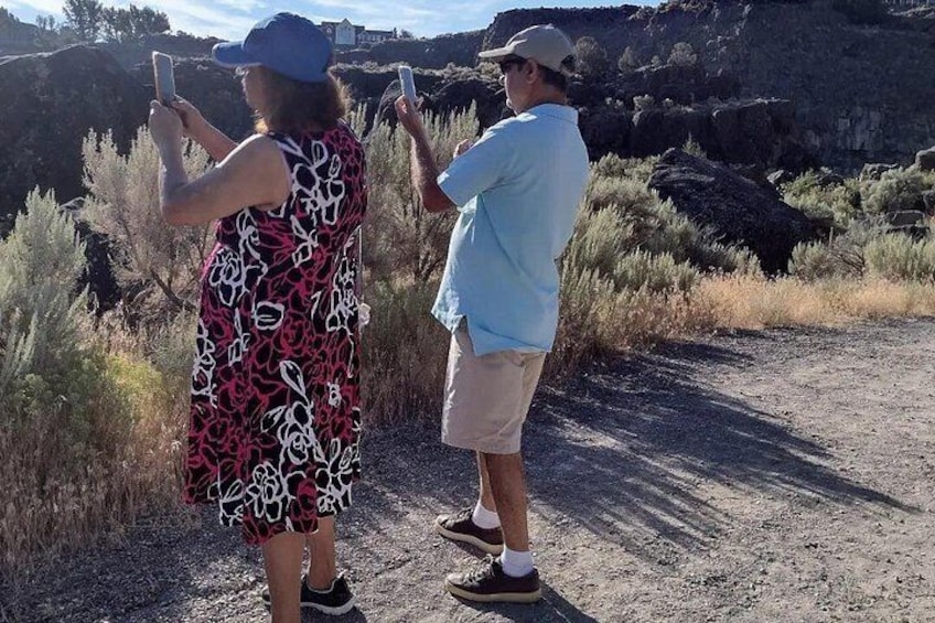 Two people taking photos with smartphones in a natural setting with dry grass and rocky terrain. 5