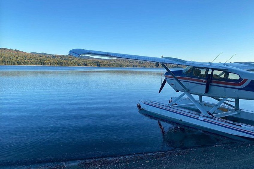 Un hydravion est garé sur un lac paisible, sous un ciel dégagé, avec des collines qui se dessinent à l’horizon. 3