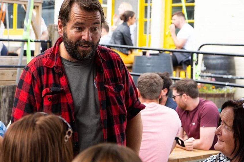 A man in a red and black checkered shirt standing in a public space with a crowd. 4