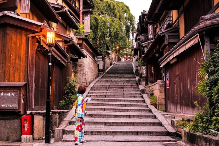 A person in colorful traditional attire standing at the base of a stone staircase in a historic town with wooden buildings and a lantern. 4