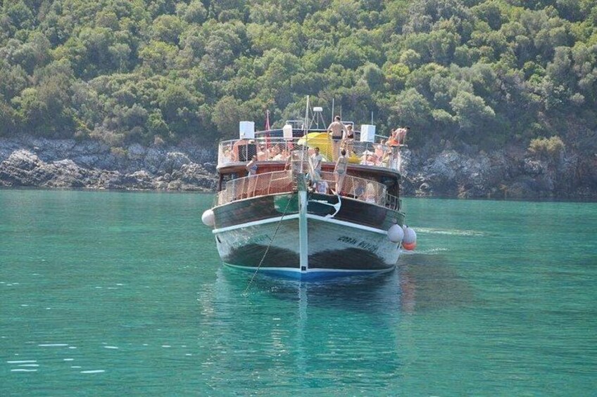 A boat with people on deck, surrounded by calm water and a forested coastline. 3