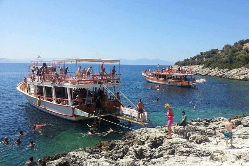 A boat with people on it, a rocky shoreline, and people swimming in the water. 5