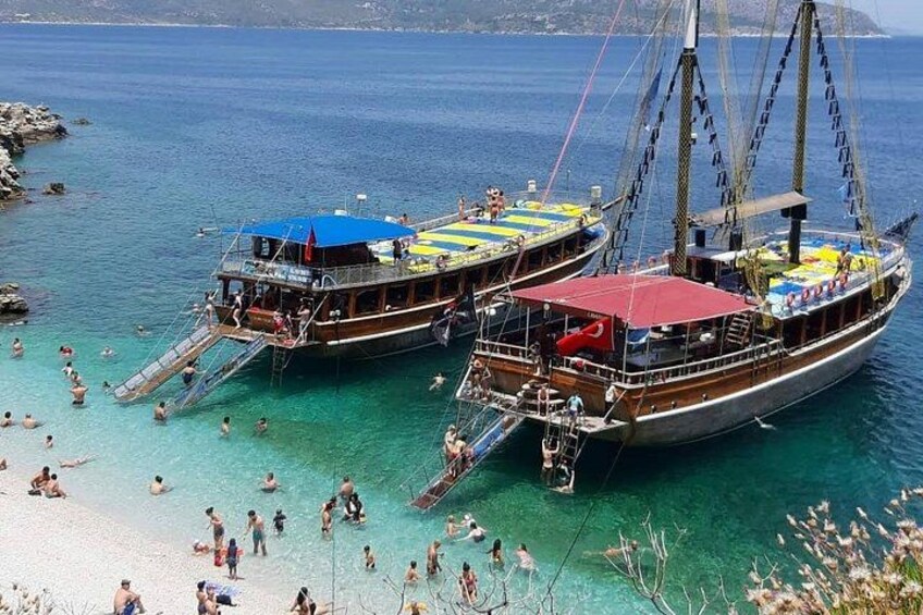 A beach with two traditional boats docked, people swimming, and a clear blue sea. 2