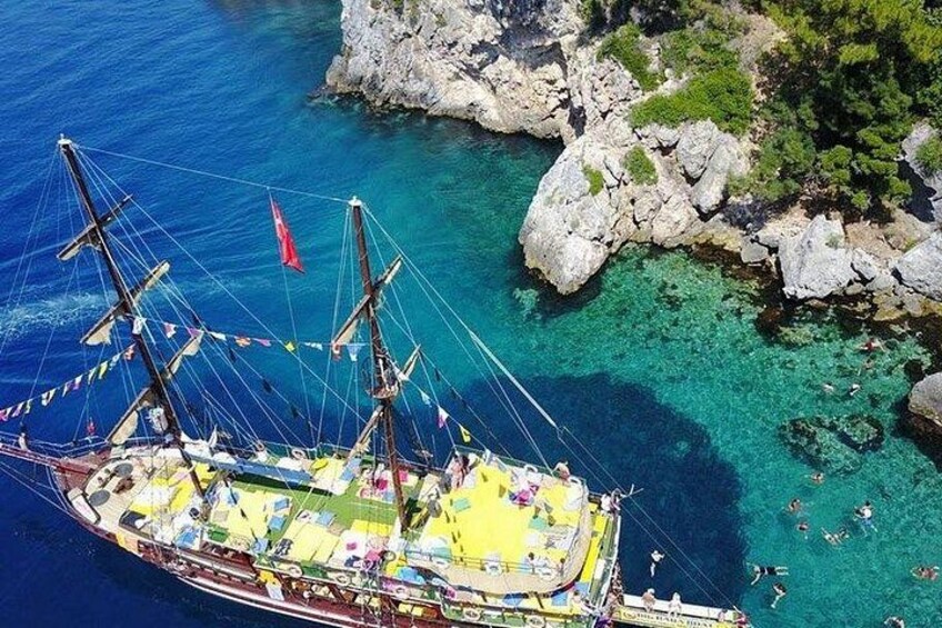 A sailboat with multiple masts and colorful decorations, anchored near a rocky coastline with clear blue water. 4