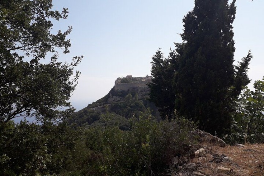 Une colline surmontée d’une fortification, bordée d’arbres denses et surplombée d’un ciel dégagé. 2
