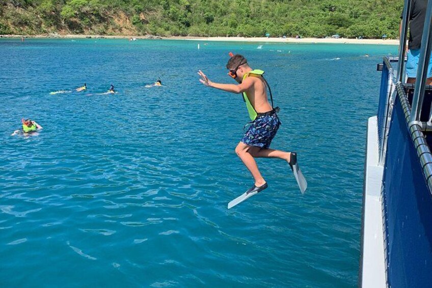 A person jumping from a boat into the water, surrounded by other swimmers. 5