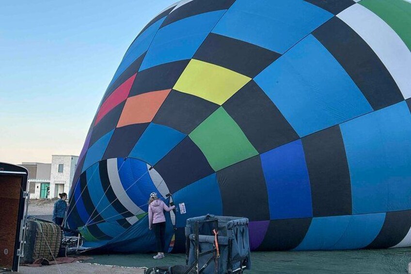 Un grand ballon à air chaud aux couleurs vives, orné d’un motif géométrique, et partiellement dégonflé, est posé sur le sol. 5