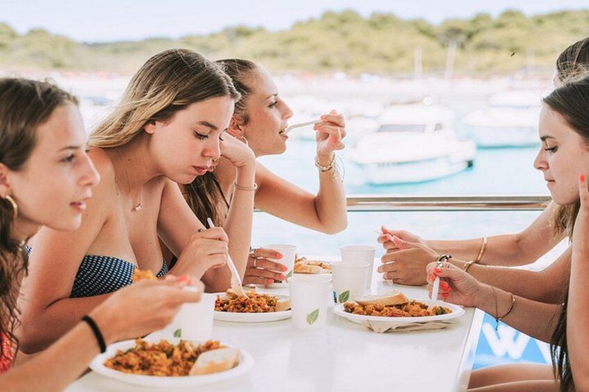 Een groep mensen dineert aan een tafel nabij een jachthaven, met boten op de achtergrond. 2