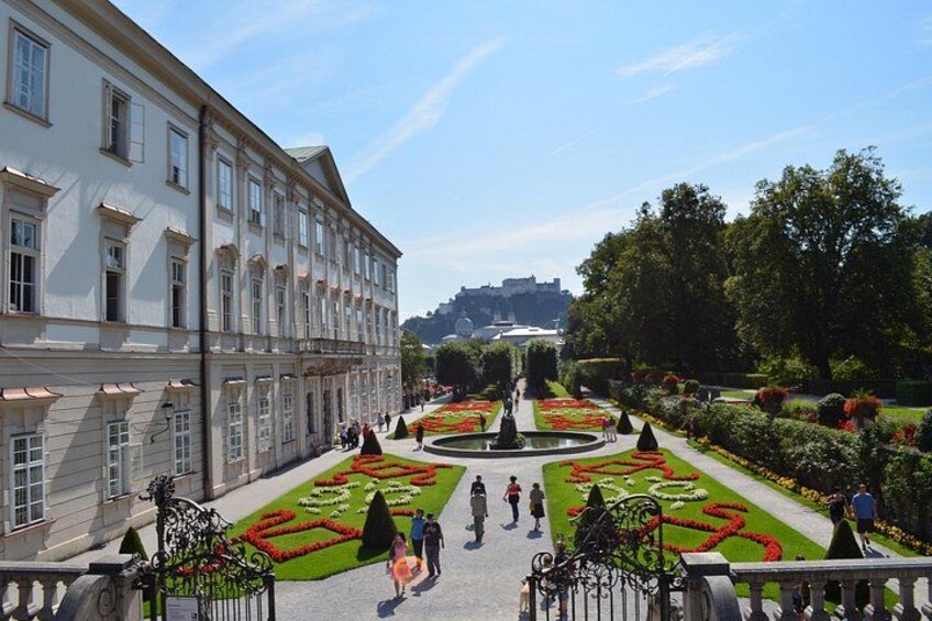 A formal garden with geometric flower beds, a fountain, and classical architecture. 4