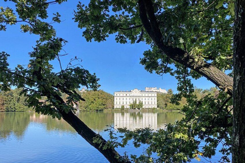 A calm lake with a reflection of a building surrounded by trees. 2
