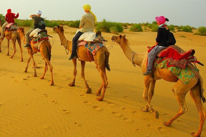 A group of people riding camels across a sandy desert landscape. 1