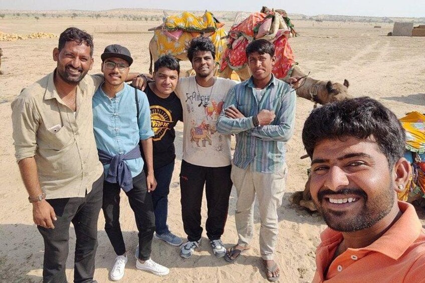 A group of people standing in a desert with a camel and a colorful cart in the background. 4