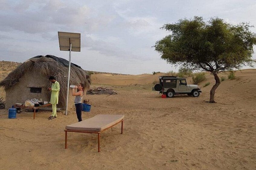 A desert landscape with a thatched-roof hut, a tree, a table, and a vehicle. 2