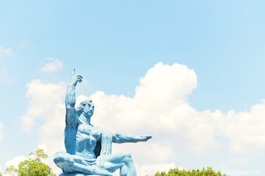 A large blue statue of a man with one arm raised, set against a clear sky with clouds. 1
