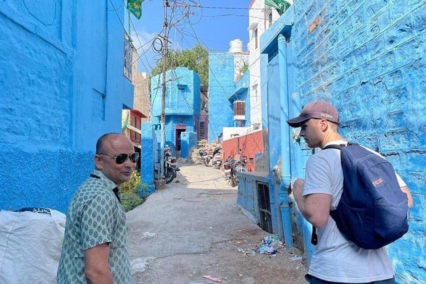 A narrow alleyway with blue-painted walls, a person with a backpack, and another person in a patterned shirt. 3