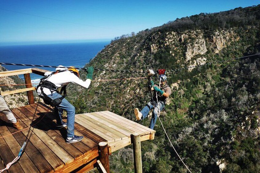 A person bungee jumping from a wooden platform with a rope, overlooking a mountainous landscape and the ocean. 1