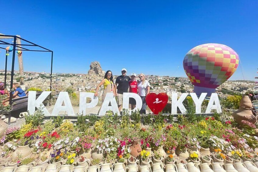 Et skilt med 'KAPADOKYA' og et hjerte, omgivet af plantekrukker og en luftballon. 1