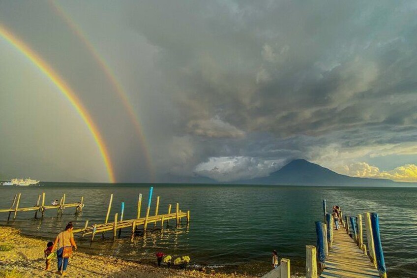 A beach with a wooden pier, a rainbow, and a mountain in the background. 2