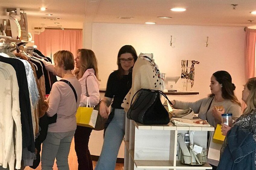 Un grupo de personas en una tienda de ropa, algunas mirando los percheros y otras sentadas en una mesa. 2