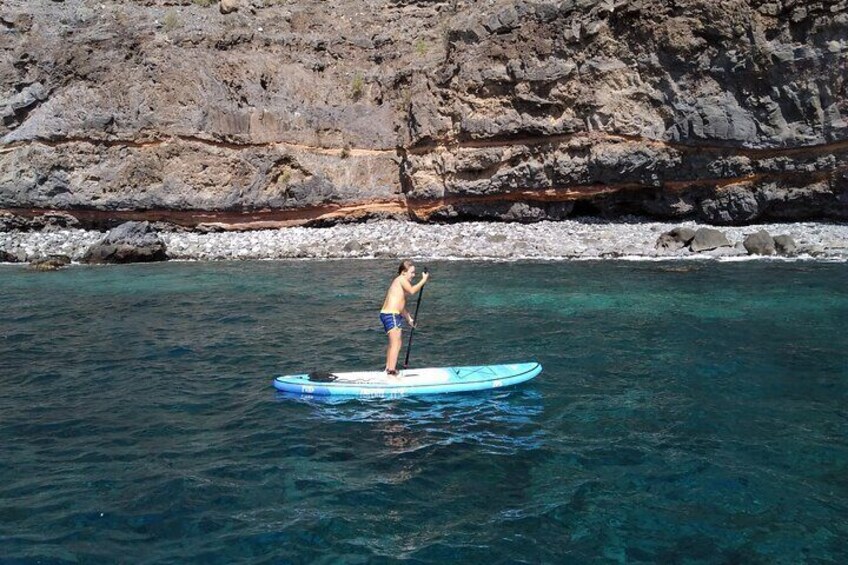 A person paddleboarding on a clear blue water body with rocky cliffs in the background. 4