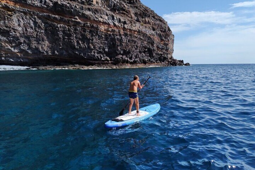 A person paddleboarding on a calm sea with a rocky cliff in the background. 5
