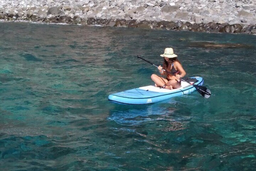 A person sitting on a blue kayak in clear water. 1
