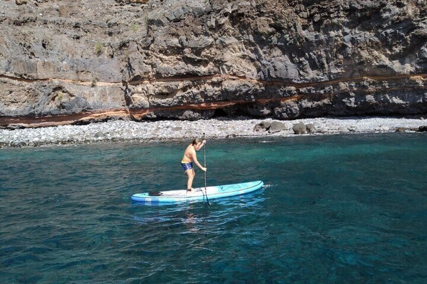 A person paddleboarding on a clear blue water body with rocky cliffs in the background. 2