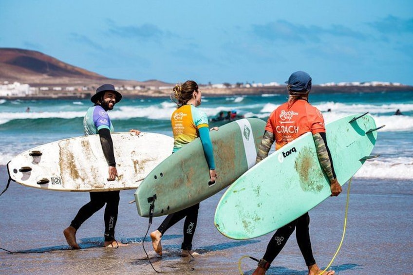 Tre persone camminano su una spiaggia con tavole da surf, onde dell'oceano e una costa in lontananza. 4