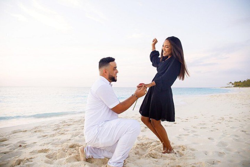 Un uomo che fa una proposta di matrimonio a una donna su una spiaggia, con sabbia e acqua sullo sfondo. 2